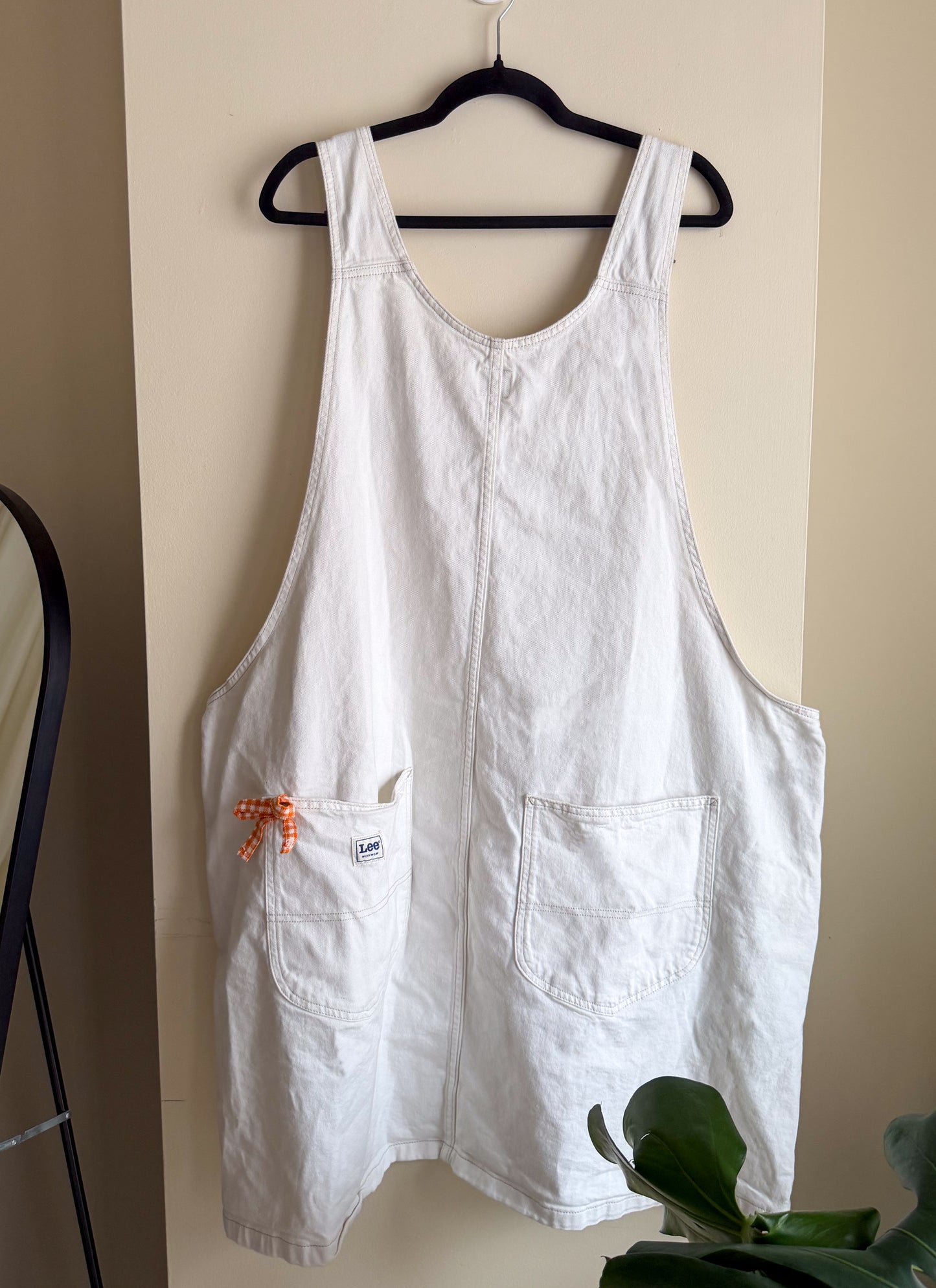 White dress hanging on a black hanger against a beige wall.