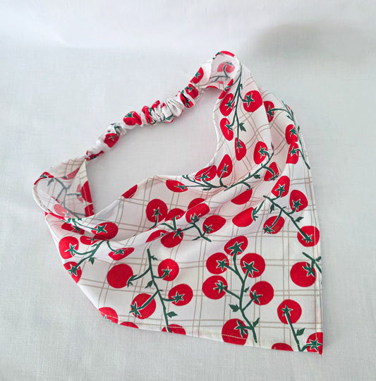 A fabric headband with a tomato print on a white background with a subtle grid pattern, laid flat on a light gray surface.
