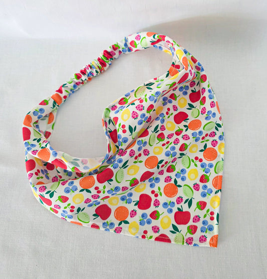 A fabric hair bandana with a colorful fruit and berry print on a white background, featuring an elasticized top edge, displayed on a light fabric surface.