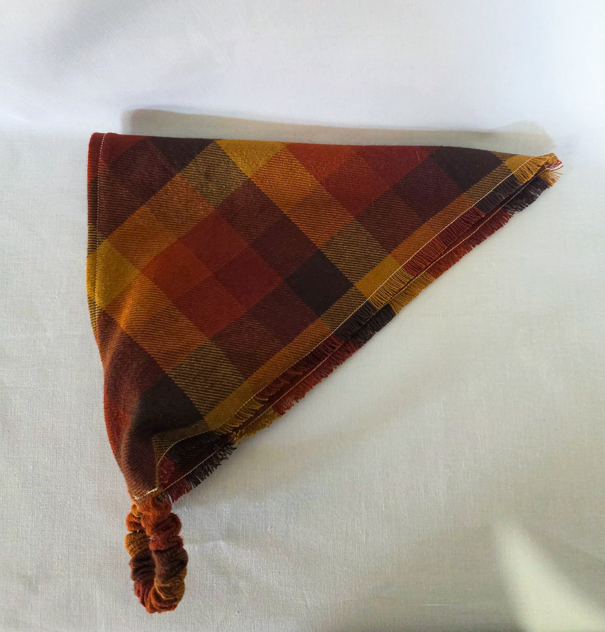 hair bandana in warm autumn colors or orange, brown, and yellow laid on its side on a white background. 