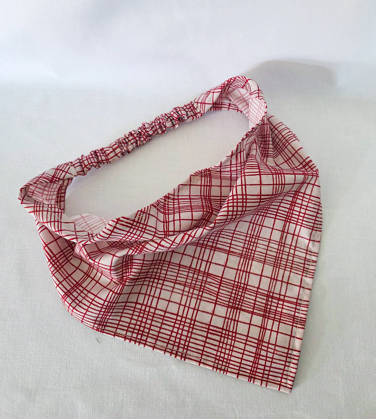 A red and white plaid hair bandana, shown laid flat on a white fabric background.