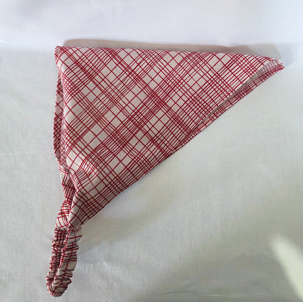 A triangular fabric bandana with a red and white plaid pattern, displayed on a white fabric background.