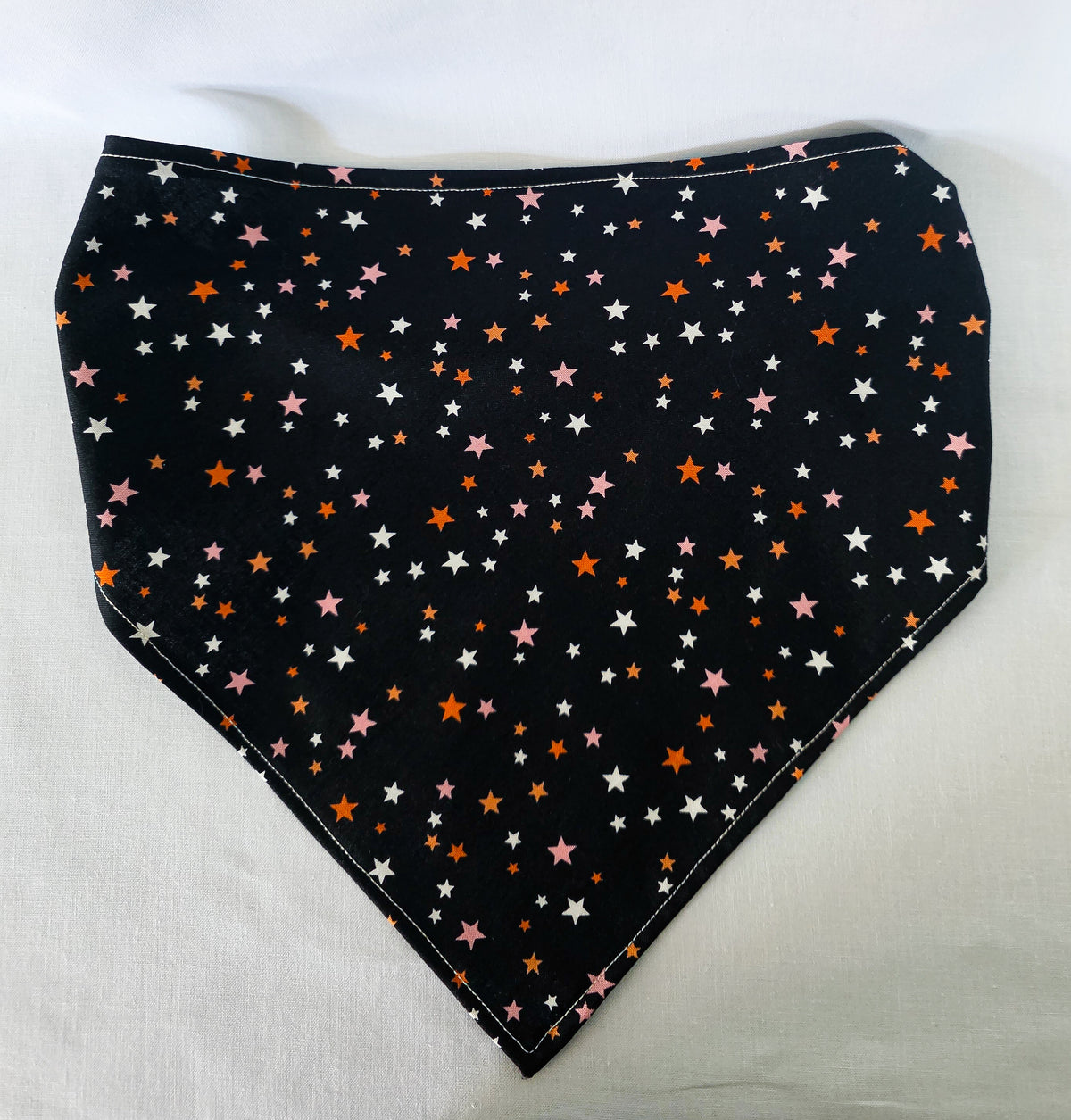 A black bandana with a scattered star pattern in orange, pink, and white, laid flat on a white fabric background.