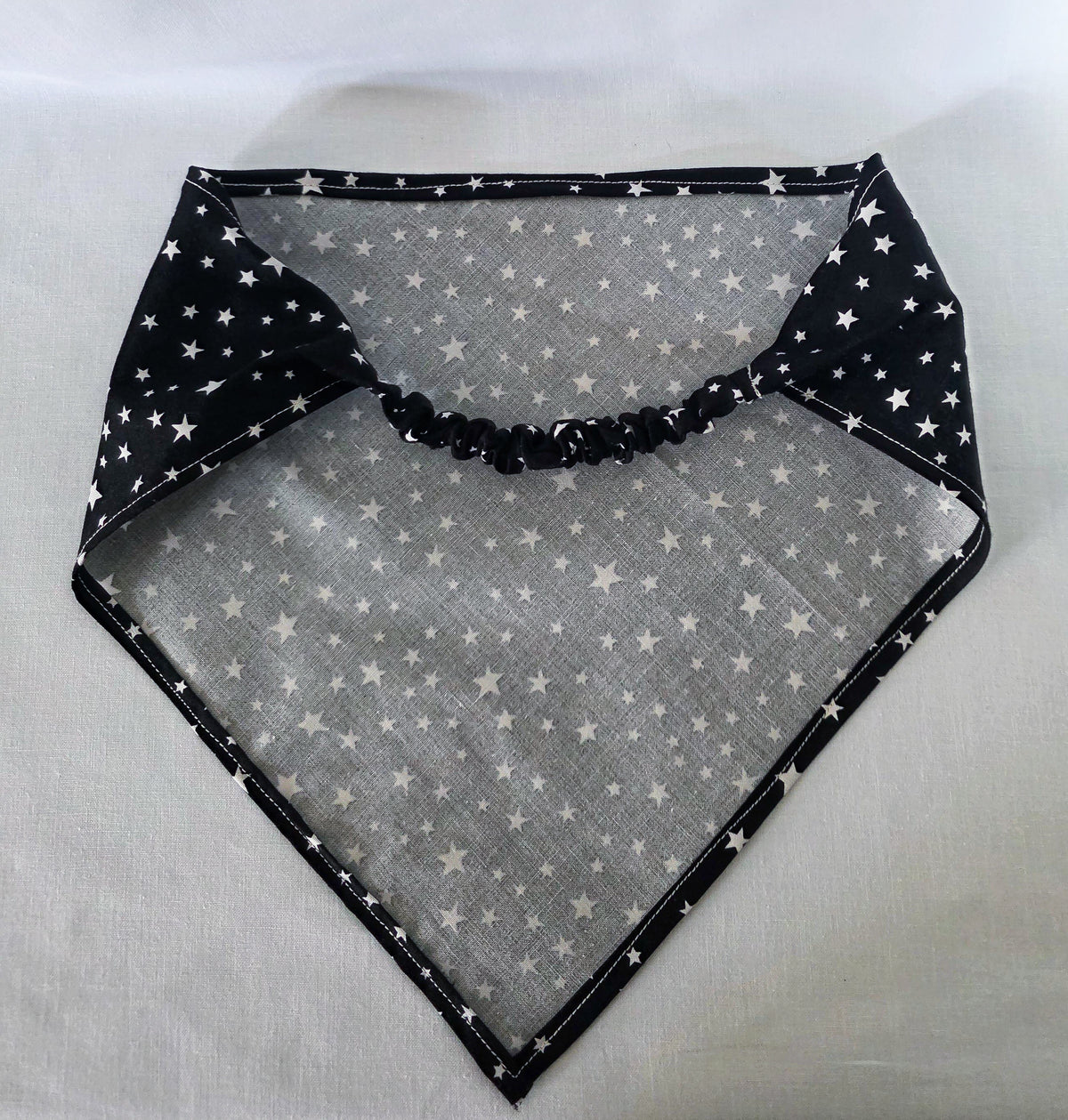 Hair bandana laid flat, showing the elastic band. It is black with white stars, and is laid on a white background. 