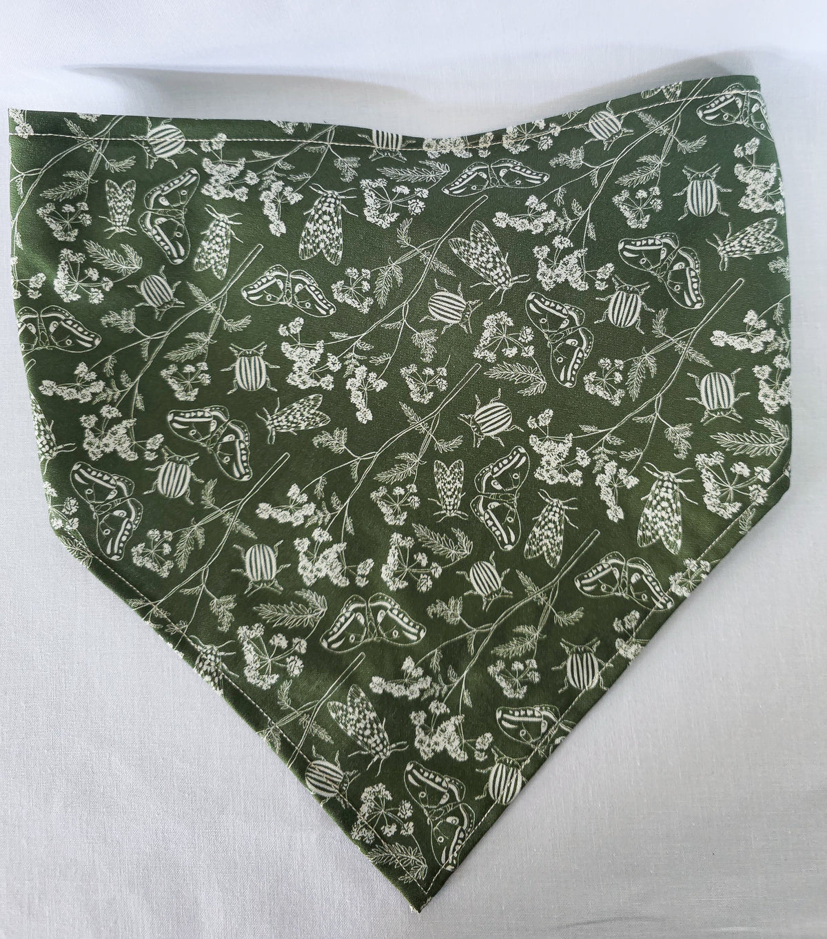 A green elastic hair bandana with a white floral and bug print on it. Laid flat on a white fabric background. 