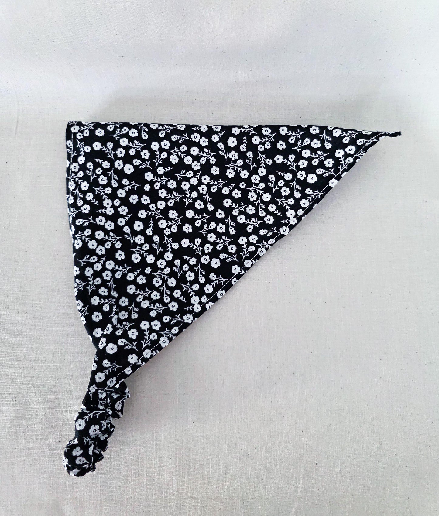 A triangular hair bandana with a black and white floral pattern displayed on a light fabric background.