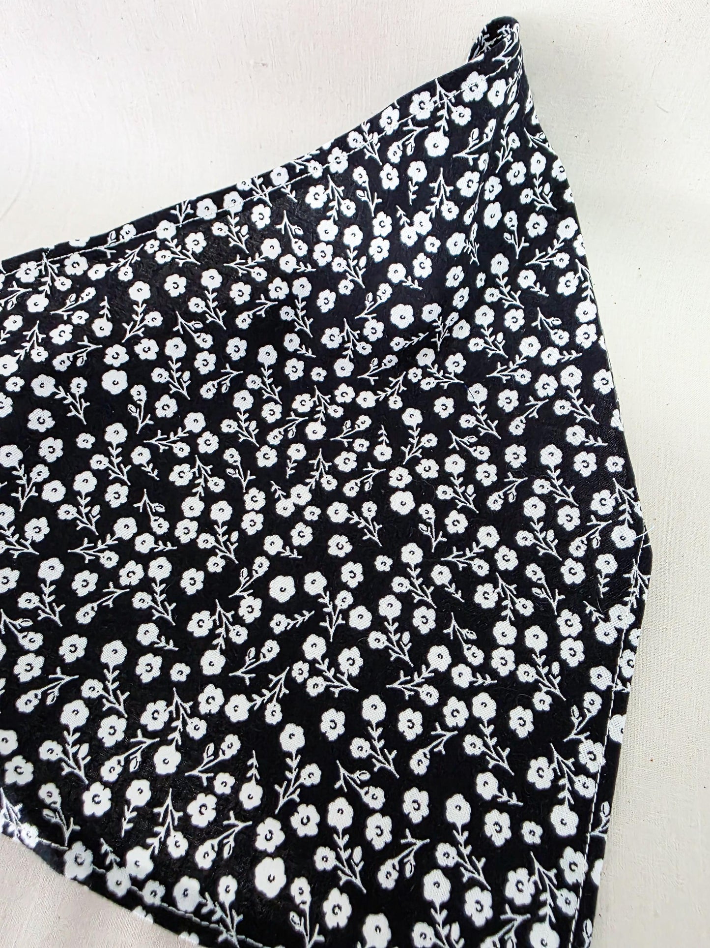 Black fabric with a dense white floral and leaf print pattern, shown folded on a light background.