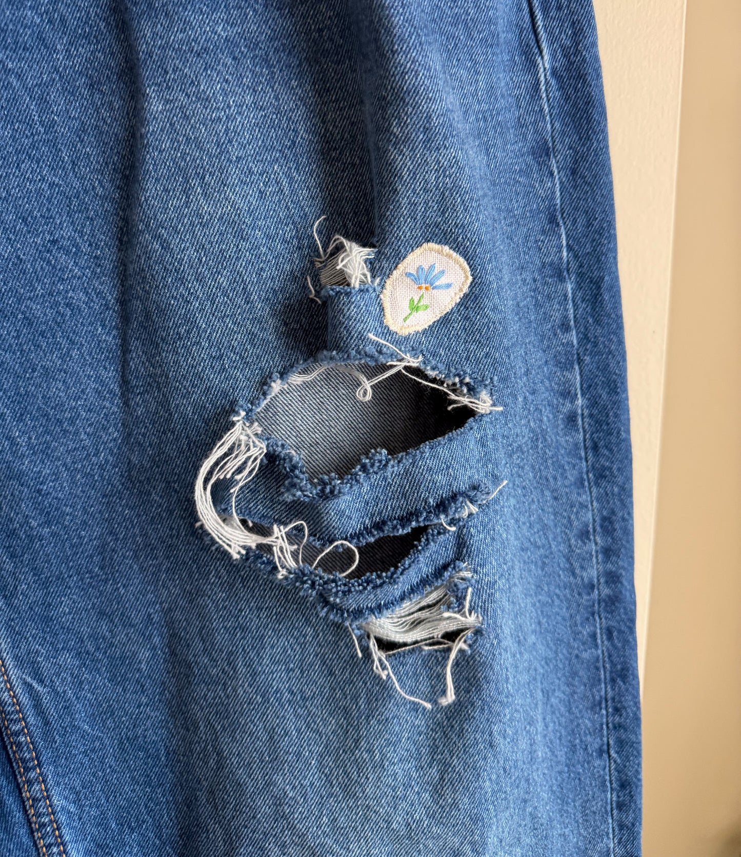 Blue denim jeans with a patch and a large rip on a beige background