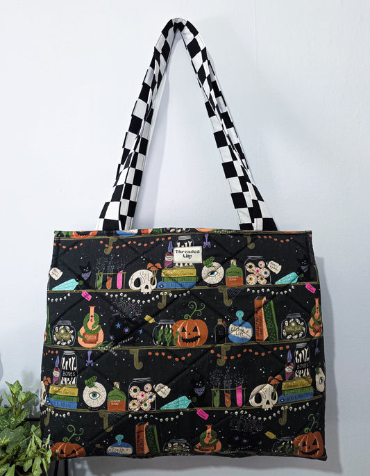 Large quilted tote bag with a witchy halloween bookshelf patterned fabric and black and white checkered straps 