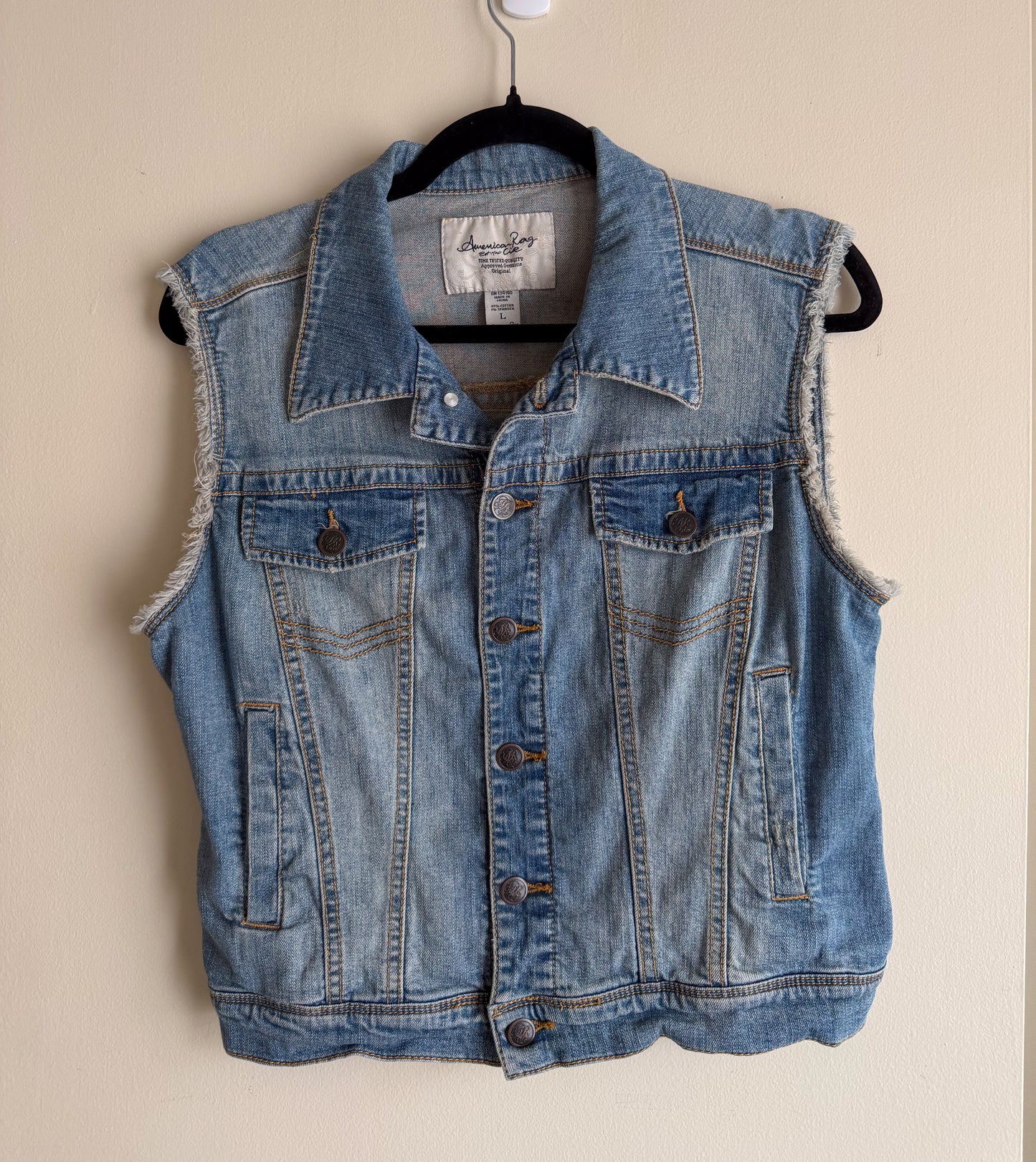 Blue denim vest on a hanger against a beige background