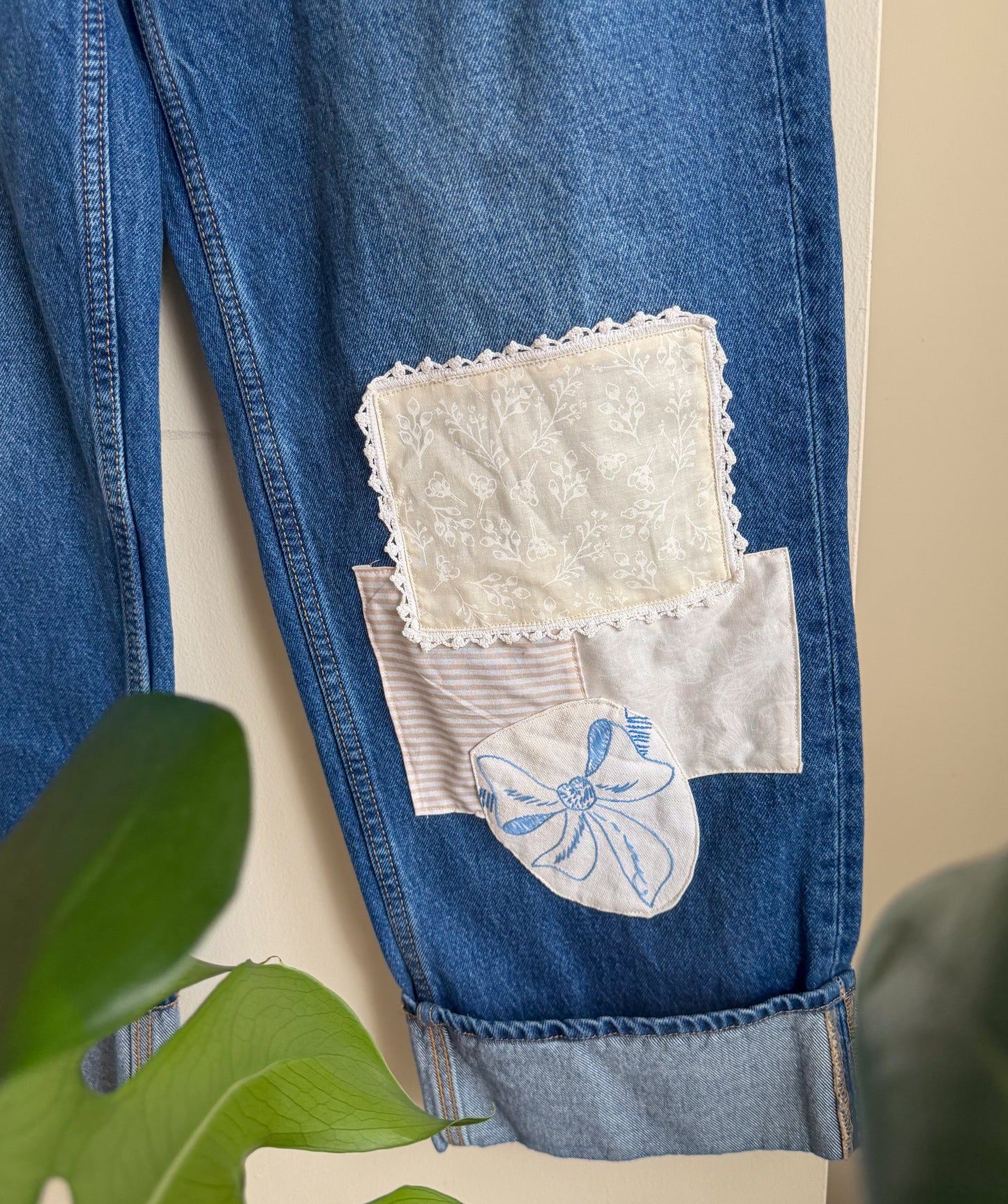 Blue denim jeans with lace and embroidered patch on a beige background