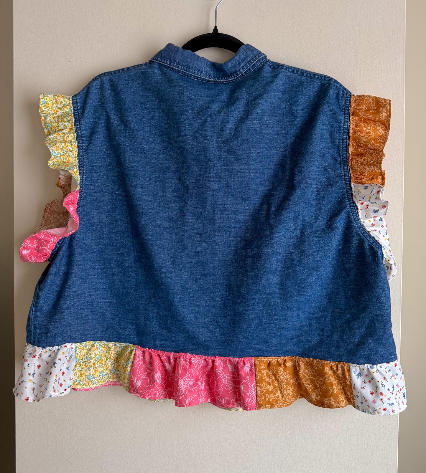 Blue denim shirt with colorful ruffled hem on a beige background