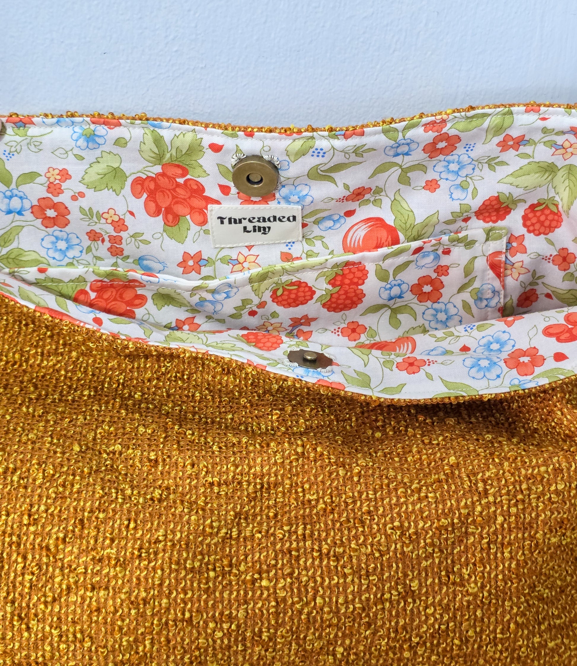 Close-up of a fabric with floral lining and textured gold exterior, featuring 'Theaded Lily' brand label.
